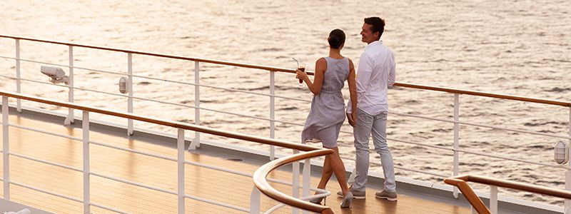 Par på kryssning som promenerar på däck i solnedgången.